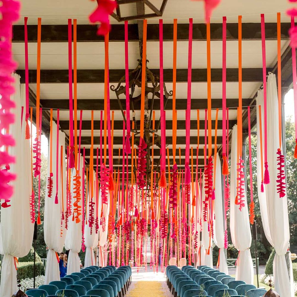 Wedding ceremony decor with hot pink and orange streamers hanging from the ceiling and flowers lining the aisle