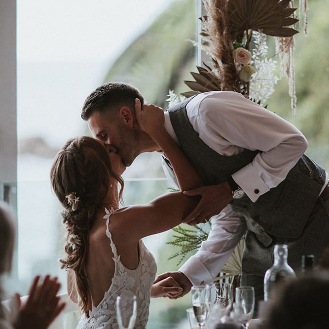 Bride & groom kiss during wedding speeches after outdoor wedding ceremony at Tunnels Beach