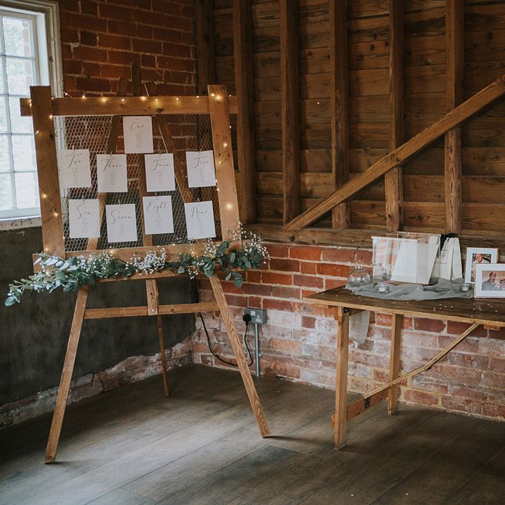 Simple wooden wedding table plan with fairy lights and a table of photographs of lost loved ones