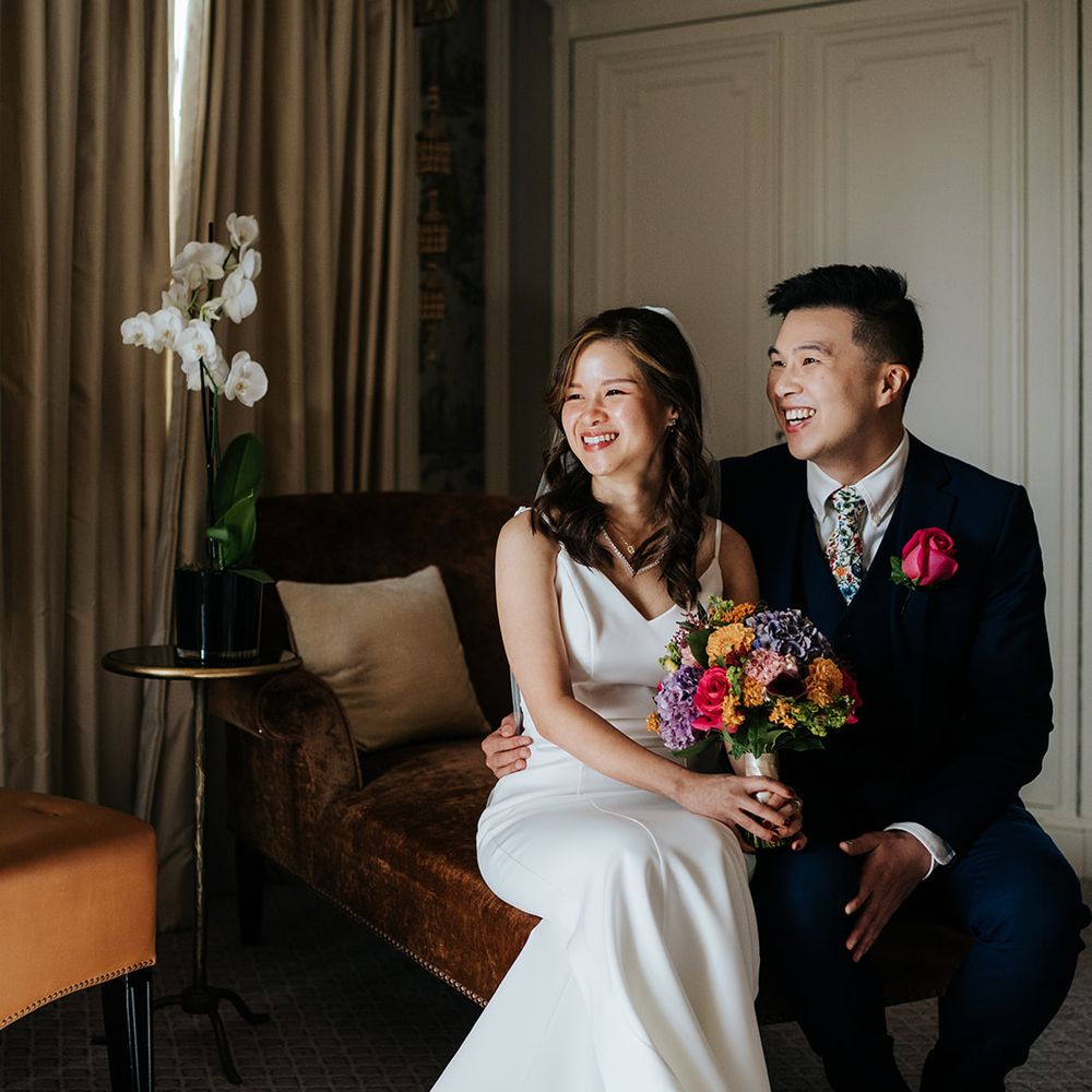 Bride holds brightly coloured floral bouquet and sits beside her groom wearing pink rose buttonhole 