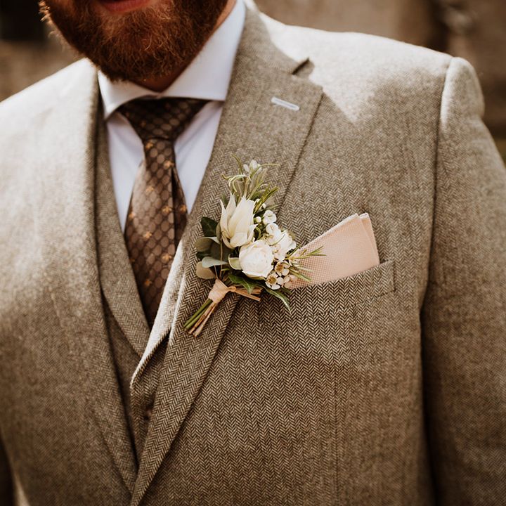 The groom in a grey tweed three piece suit with a pink pocket square and white flower buttonhole 