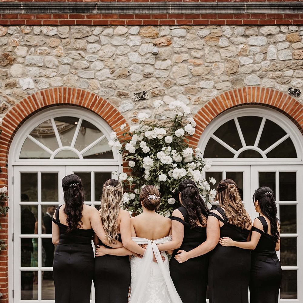 The bride in a lace wedding dresses poses with her bridesmaids in one shoulder black dresses for a traditional wedding 