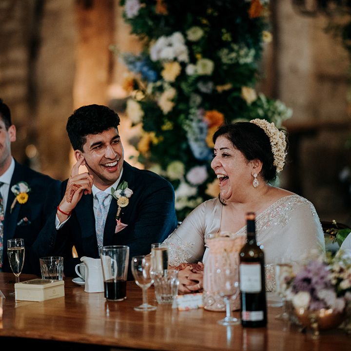 Grooms sit with wedding guests at banquet head table during barn wedding reception 