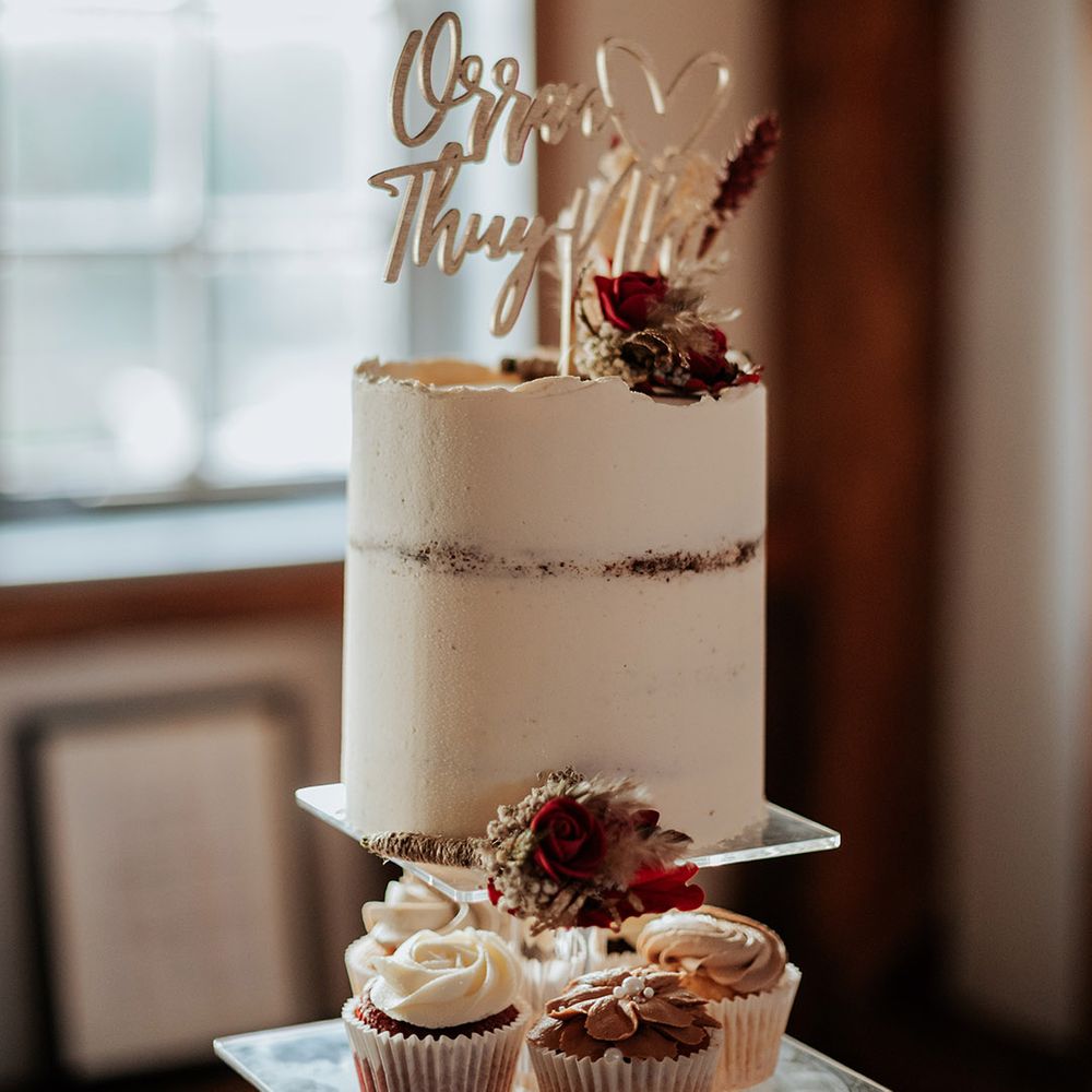 Rustic white frosted wedding cake with red rose and dried flower decor with wooden laser cut cake topper and cupcakes 