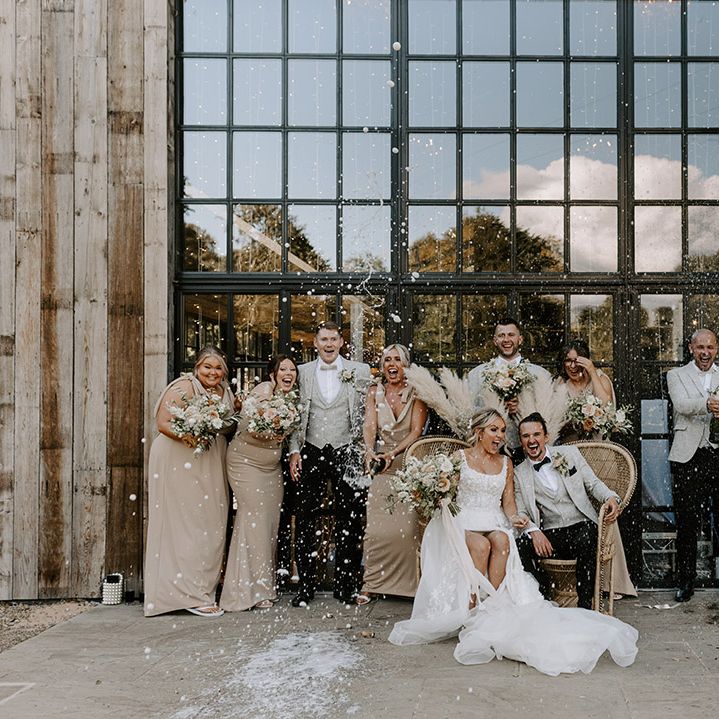 The bride and groom sit on boho peacock chairs as the wedding party pop champagne at Hidden River Cabins 