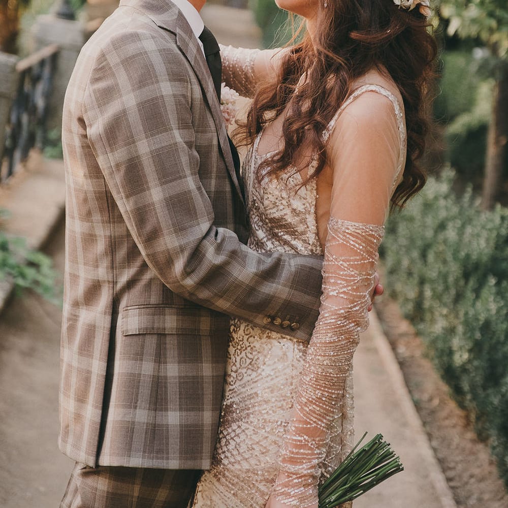 Spanish destination wedding with groom in a grey check suit embracing his bride in a bespoke sparkly wedding dress