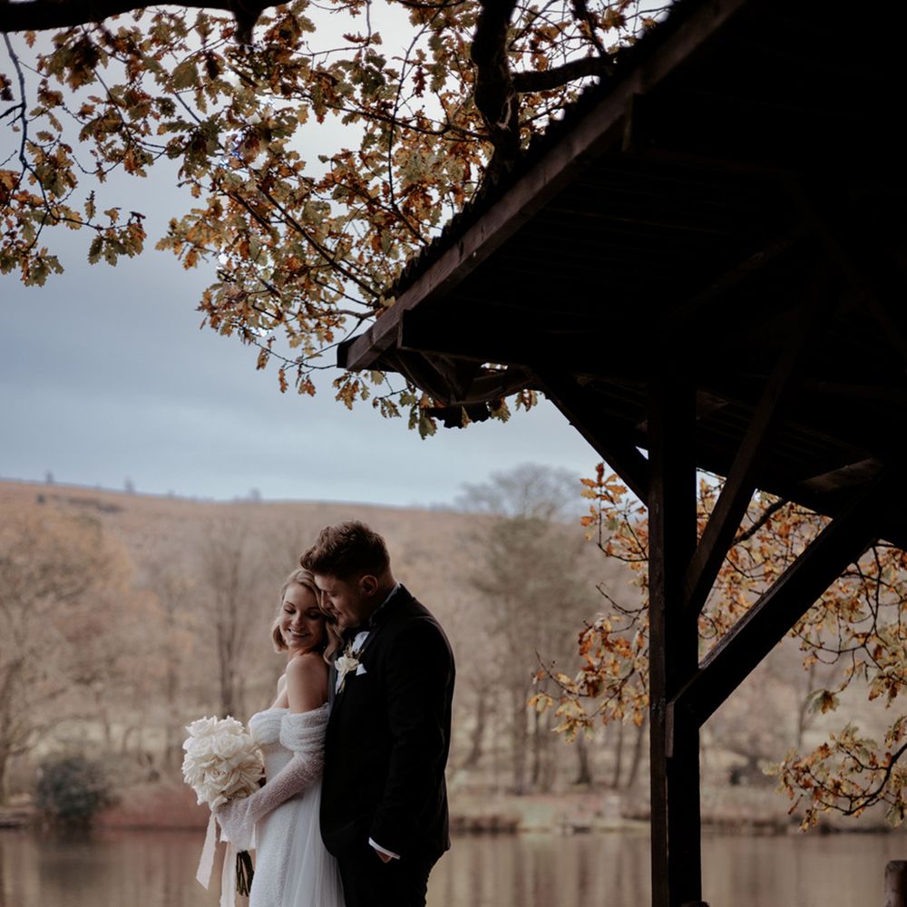 The bride and groom stand closely together looking out over a lake at Wyresdale Park wedding venue 