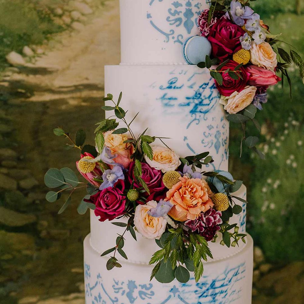 Four tiered toile wedding cake in blue and white with spring flower decorations and blue macaroons 