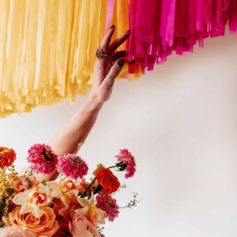 Bride with silver wedding jewellery holding colourful mixed floral bridal bouquet touching yellow and pink wedding streamers at Northern Monk Refectory Leeds