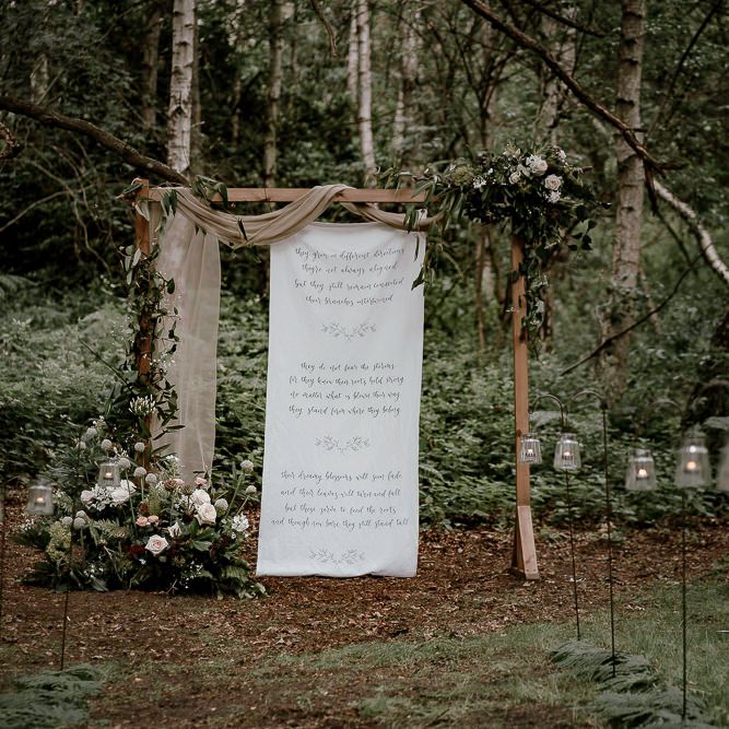 Wooden frame int he woods decorated with drapes, flowers and fabric sign