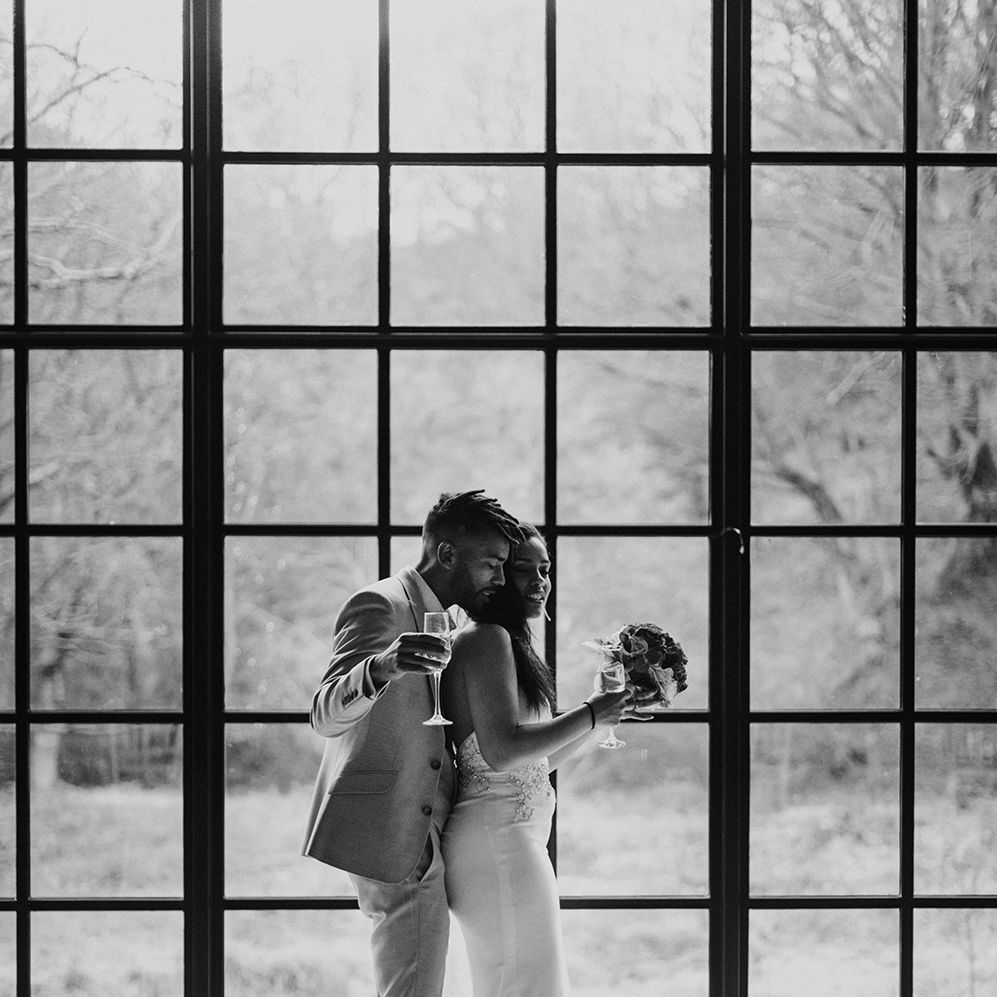 Black & white image of bride & groom dancing on their wedding day in front of arched window