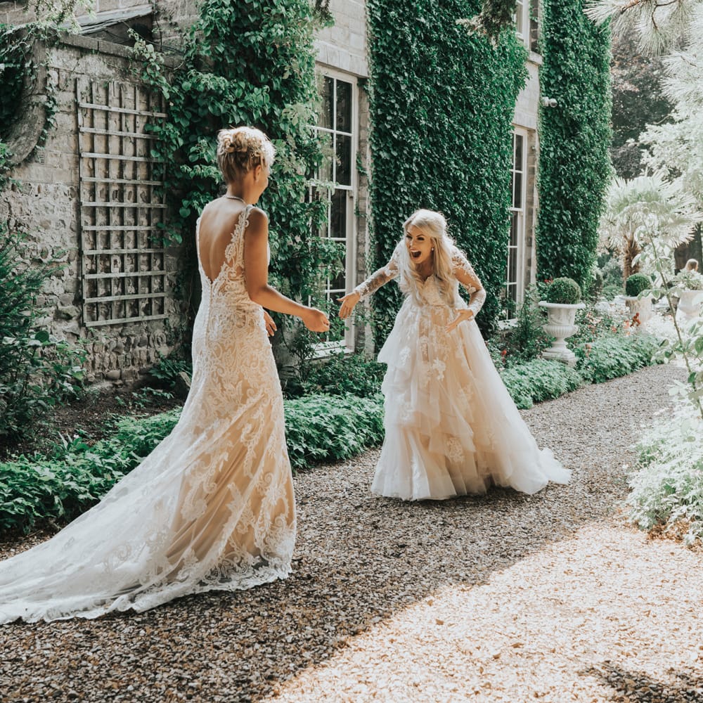 Two brides engage in a 'first look' before their wedding ceremony. They are laughing with mouths open.