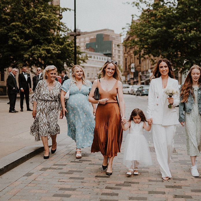 Bride in a white bridal suit and female guests walking through the streets of Sheffield