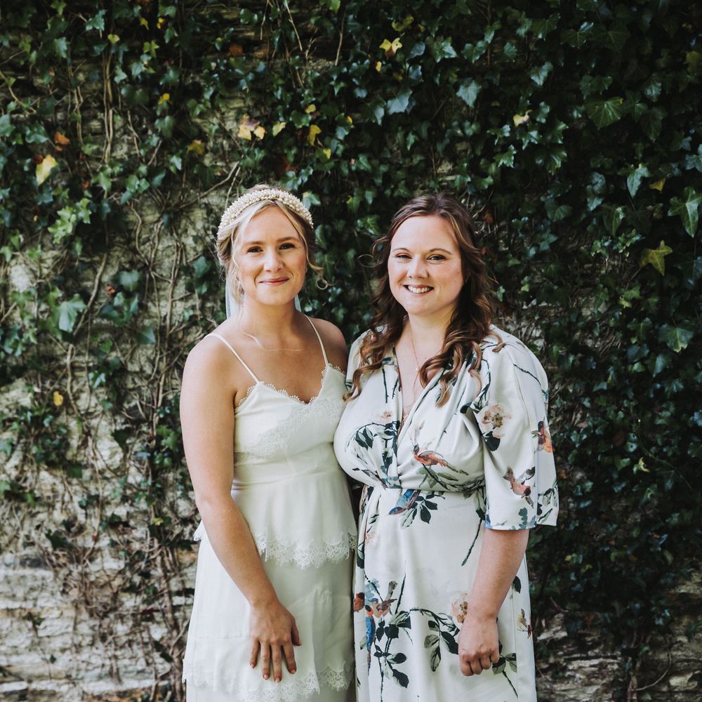 Bride stands with her bridesmaid on her wedding day, bridesmaid wears floral dress 