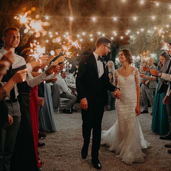 Bride & groom walk underneath fairy light canopy as wedding guests stand around them | Royal Studio