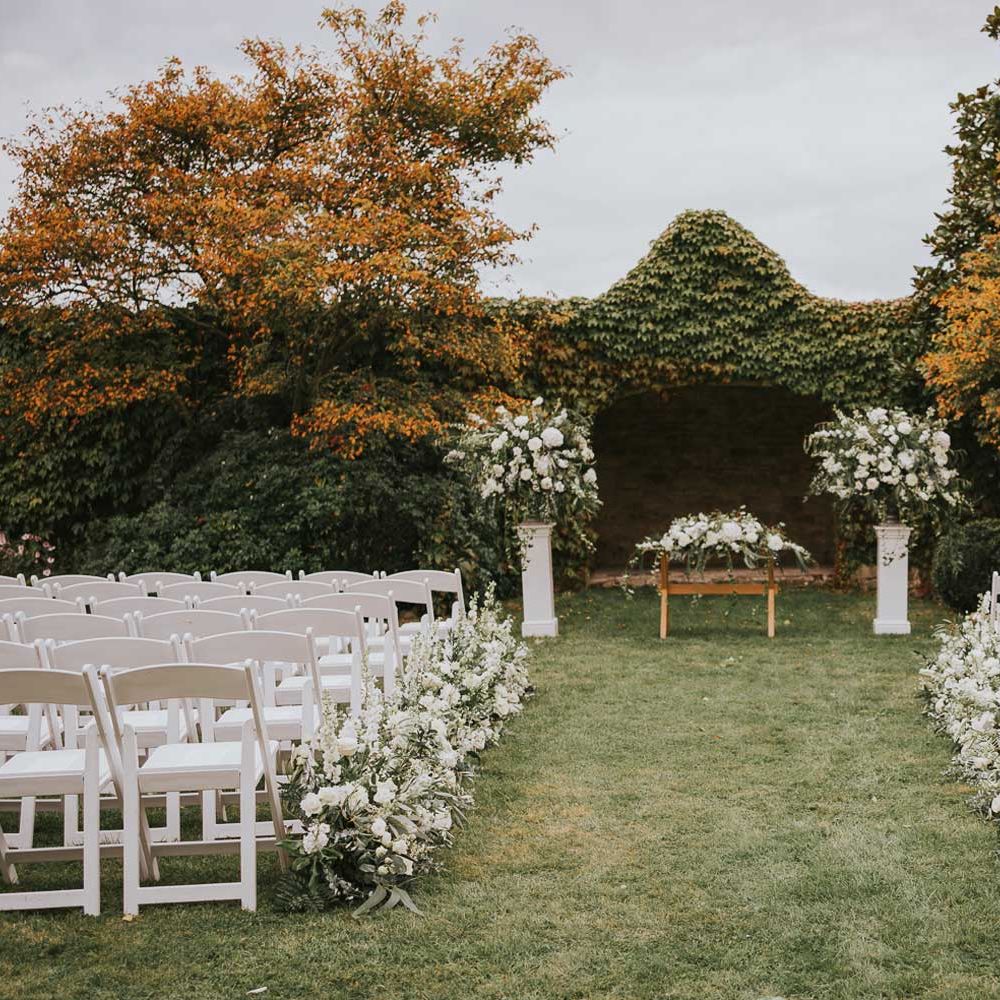 White wooden chairs, green and white flowers and outdoor aisle for outdoor wedding ceremony at Notley Abbey