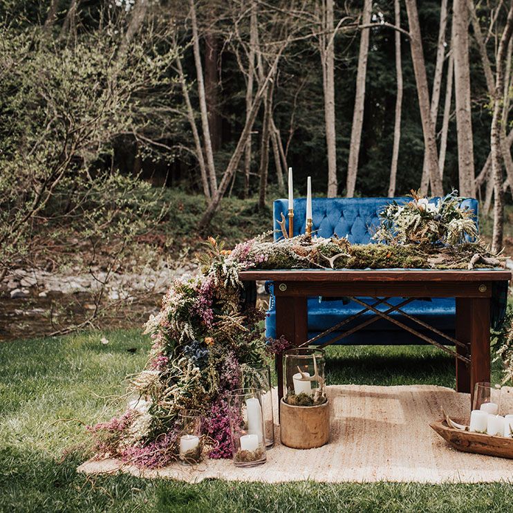 Outdoor sweetheart table with plush blue velvet love seat and trailing wild flower arrangement 