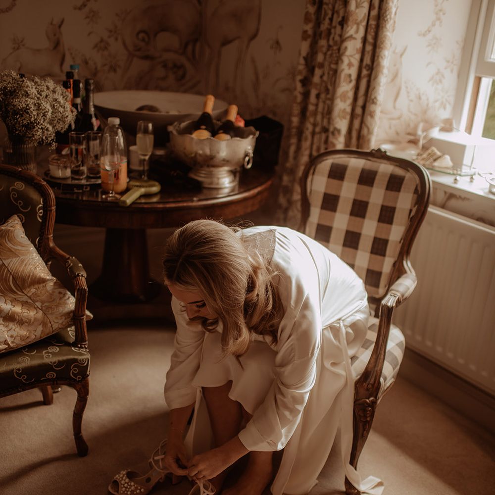 Bride in a satin getting ready robe putting on her pearl Charlotte Mills wedding peep toe wedding shoes 
