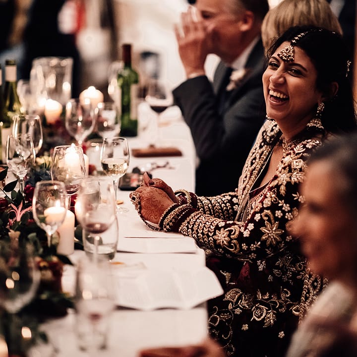 Bride smiles at wedding table with tall wine glasses and sequin jewellery pieces
