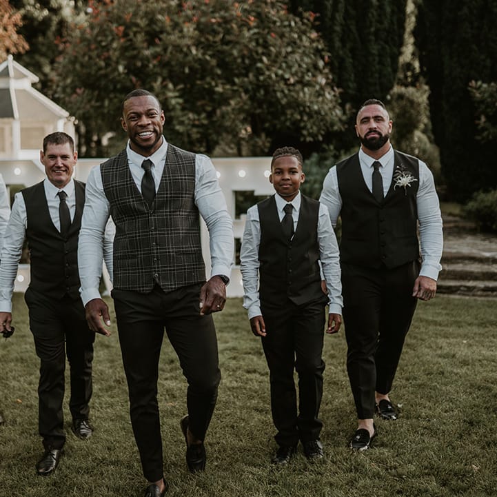 Groom smiles as he wears tartan waistcoat complete with green trousers and walks with his groomsmen 
