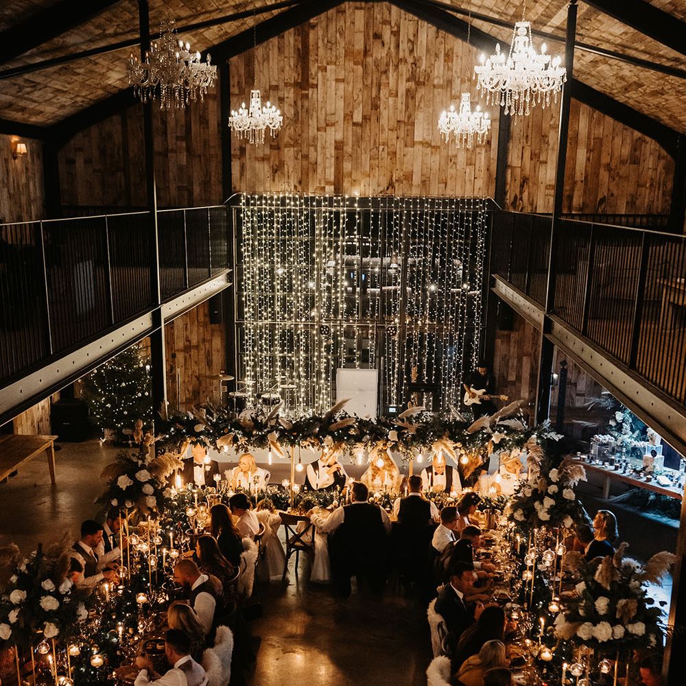 Wedding guests sit down to candle lit Christmas feast with festive decor and fairy lights 