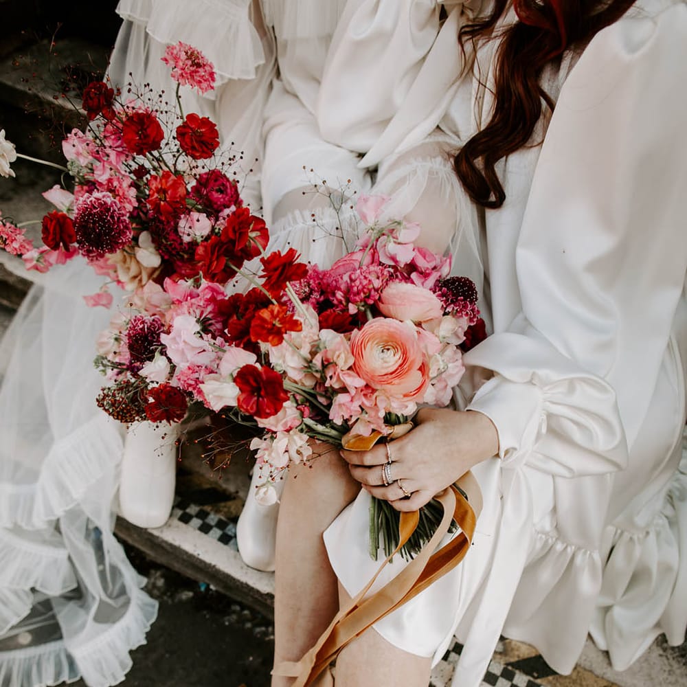 two brides holding red and pink bouquets with sweet peas and butterfly ranculus 