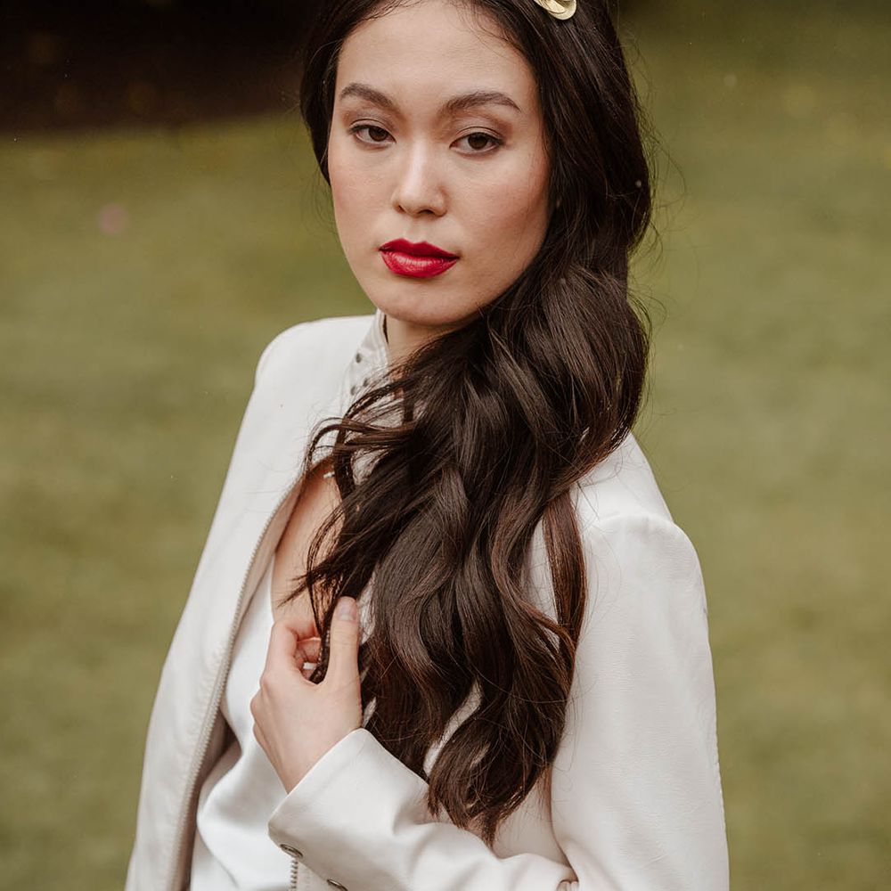East Asian bride in a white bridal coverup and satin slip wedding dress with long wavy hair and red lipstick