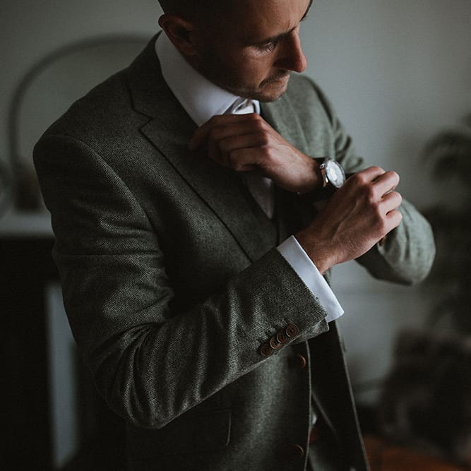 Groom wears three piece suit as he does up his cufflinks on the morning of his wedding day