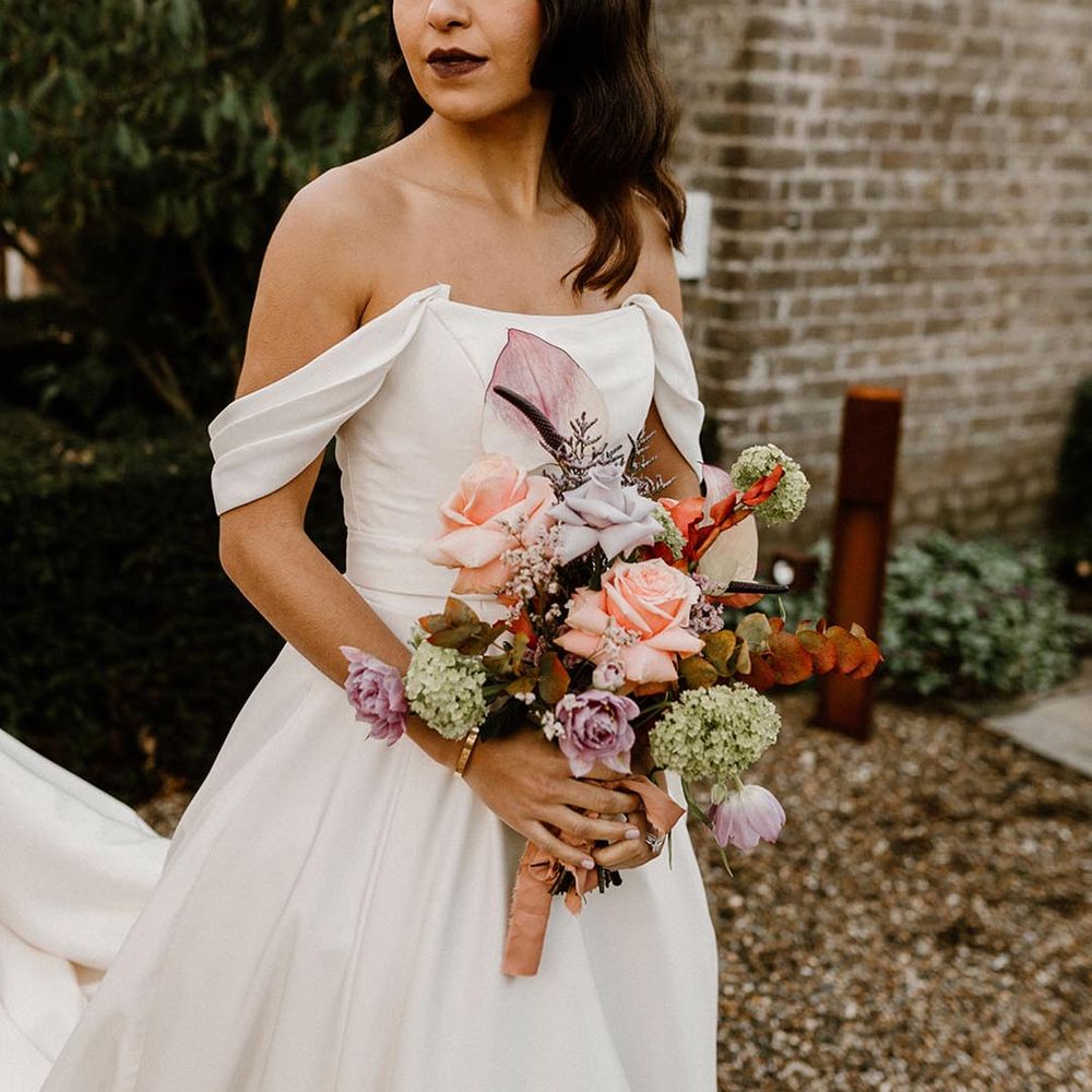 Bride with a dark lip wears an off the shoulder wedding dress holding an autumnal wedding bouquet 