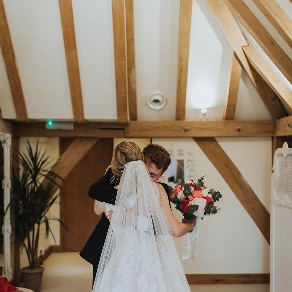 Bride wearing a floral lace wedding dress hugging family member as they get their first look at the bride 