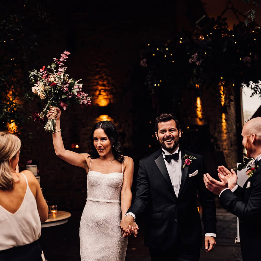 Groom in a classic black tuxedo walks back down the aisle with the bride in a beaded sparkle wedding dress 