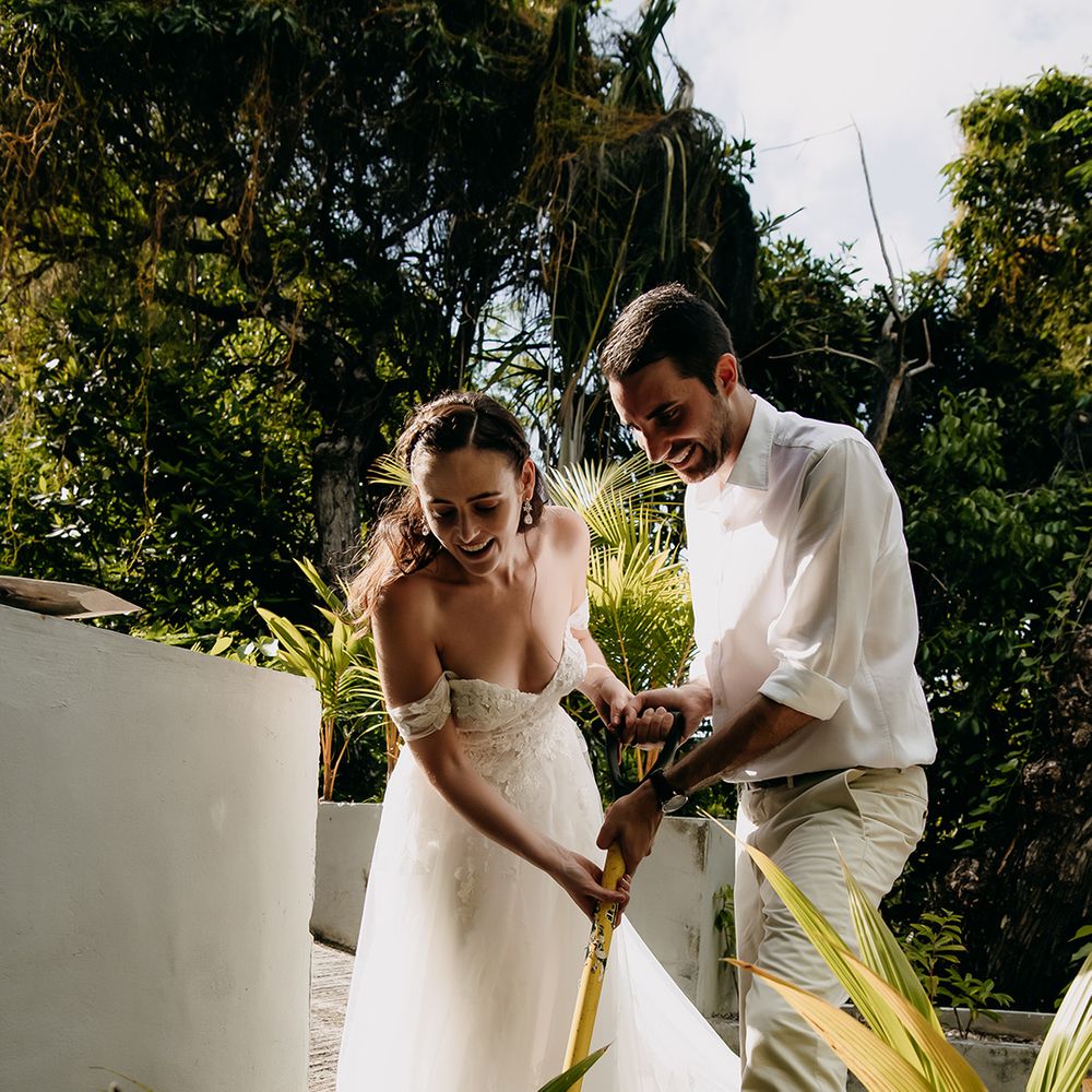 Bride and groom both holding gardening shovel planting small tree and personalised engraved plant stick