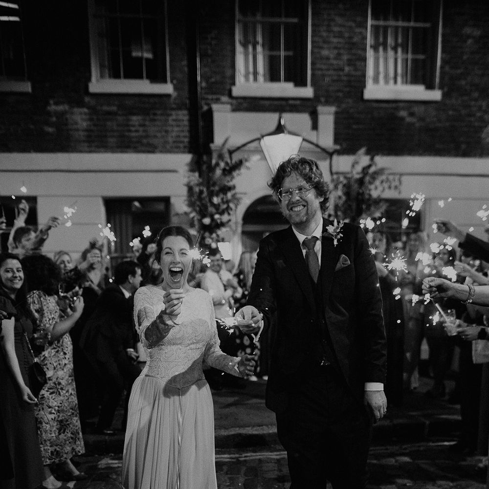 Groom in dark suit with orange tie and autumnal boutonniere and bride in long sleeve lace vintage wedding dress and closed toe satin heels doing sparkler exit from autumnal intimate London wedding