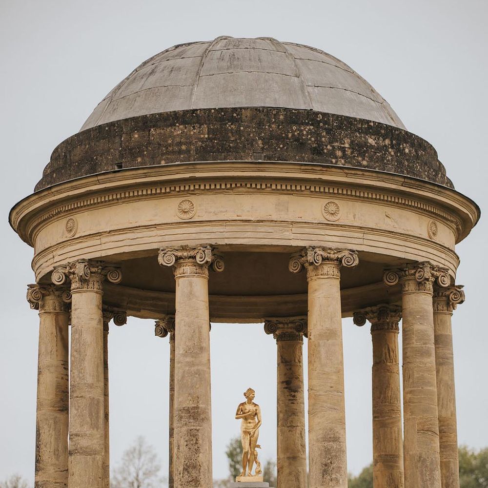 The bride and groom share a kiss as they lean against the incredible architecture at Stowe House wedding venue 