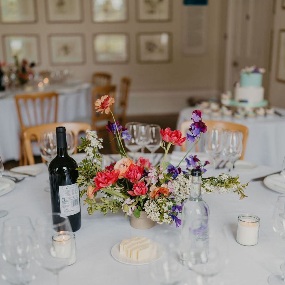Brightly coloured floral centrepieces on round tables covered with white tablecloths 