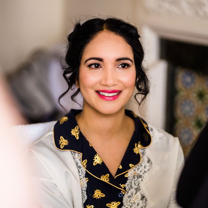 Bride wears fuchsia pink lipsticks and her dark hair tied into up do with curled tendrils to the front 