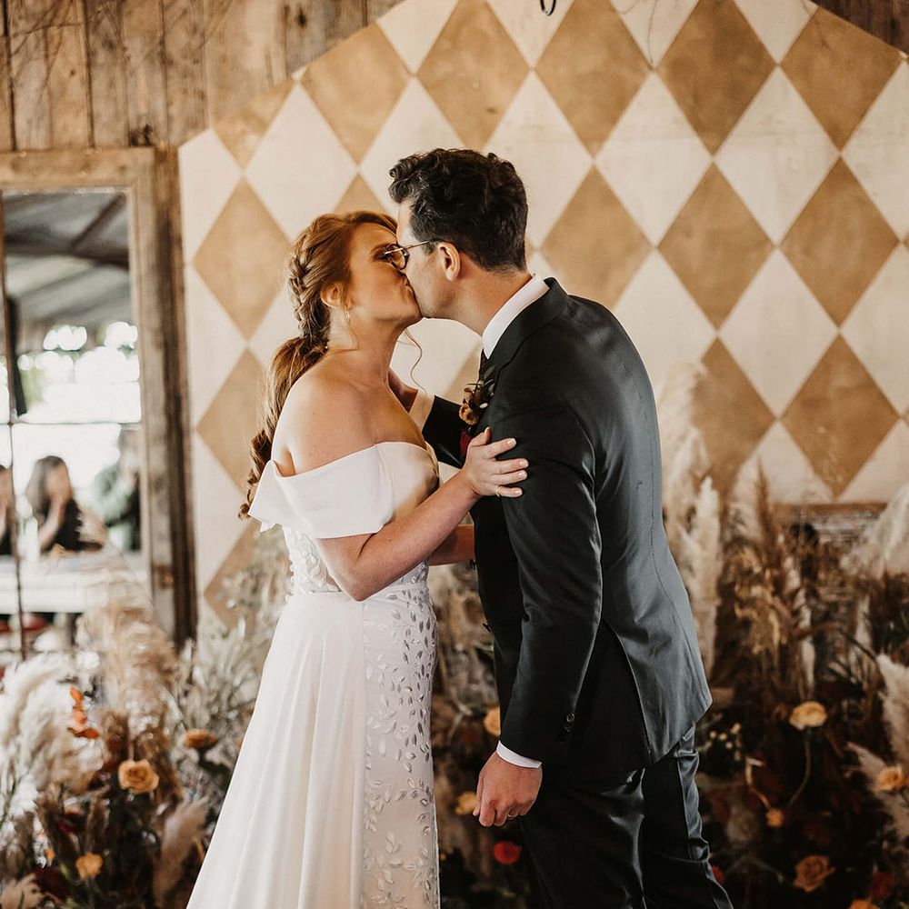 Bride in off the shoulder Love Spell wedding dress kisses her groom during barn wedding with Autumnal styling 