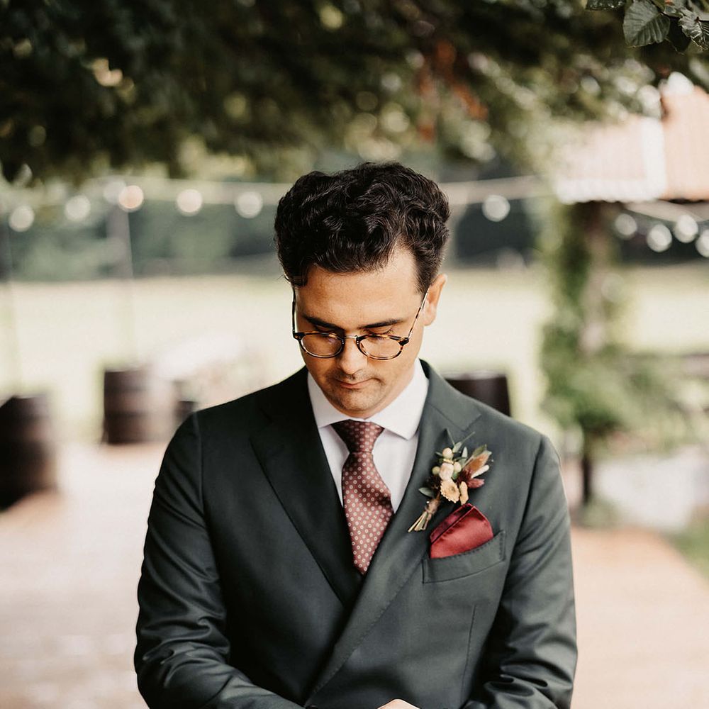 Groom wears bespoke Suit Supply suit complete with silk red pocket square and floral buttonhole