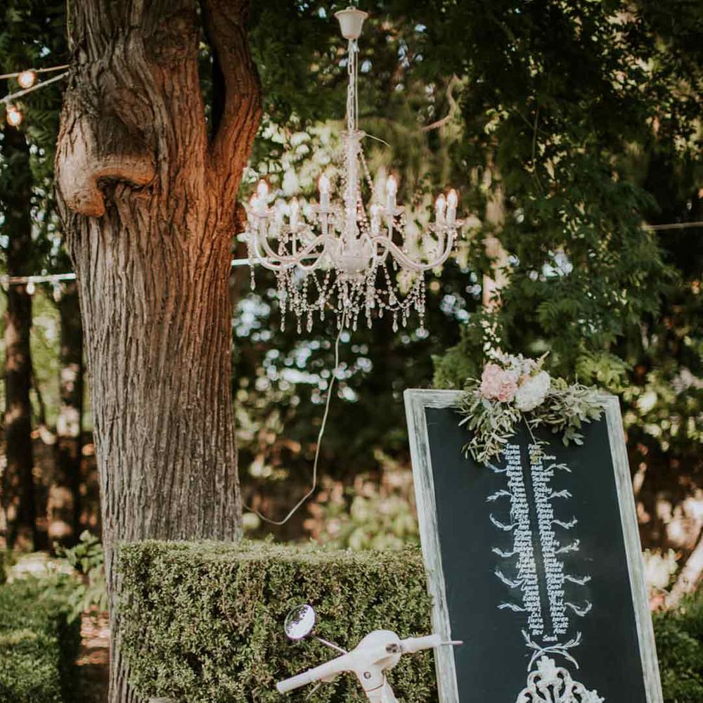 White wedding moped underneath a chandelier and next to large chalkboard wedding sign 
