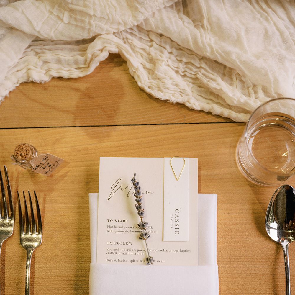 White wedding menu with wedding place name attached with gold paperclip with sprig of lavender and white napkin with silver cutlery
