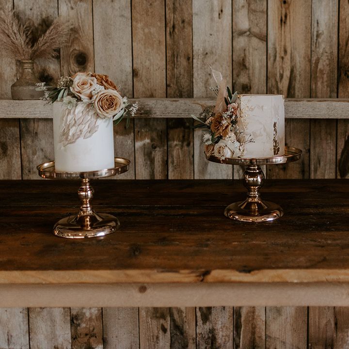 Three small single tier white iced wedding cakes in round, hexagonal, and square shapes with pale pink frosting and floral decor on gold cake stands