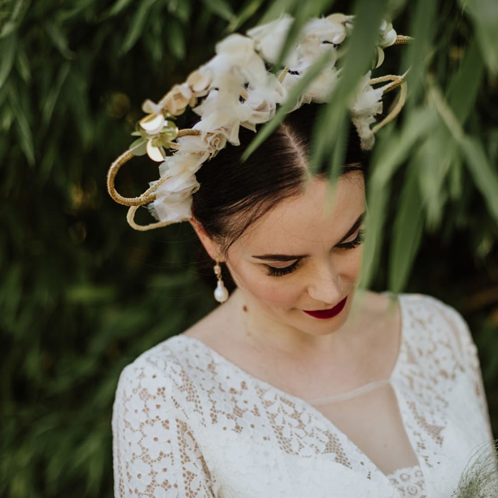 Structured bridal crown with white floral detailing on bride in lace wedding dress and red lip makeup