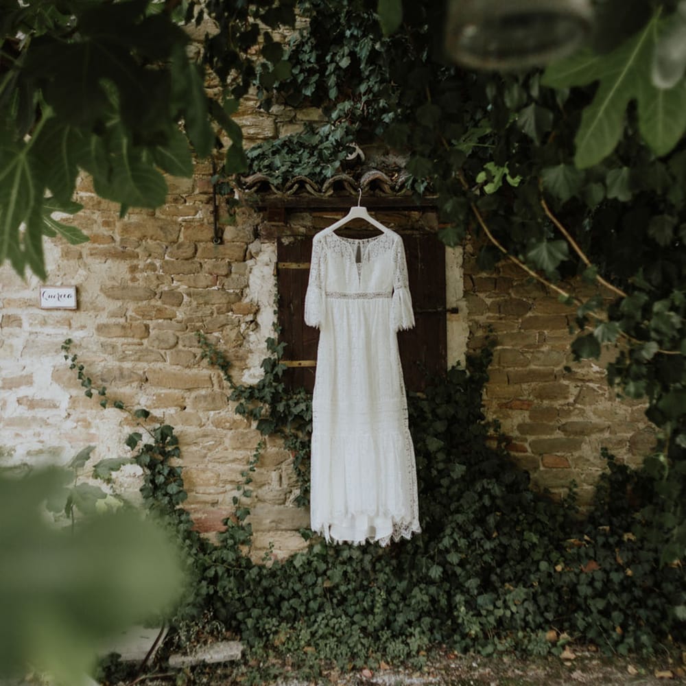 lace wedding dress hanging outside a rustic italian wedding venue surrounded by greenery