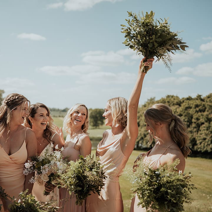 Bridesmaids in mismatched style bridesmaid dresses holding up their own green foliage bouquets 