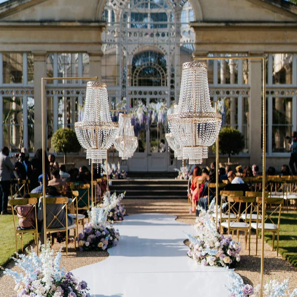 Syon Park wedding venue with outdoor gold and crystal chandeliers and pastel aisle flower arrangements outside of The Great Conservatory for vow renewal 