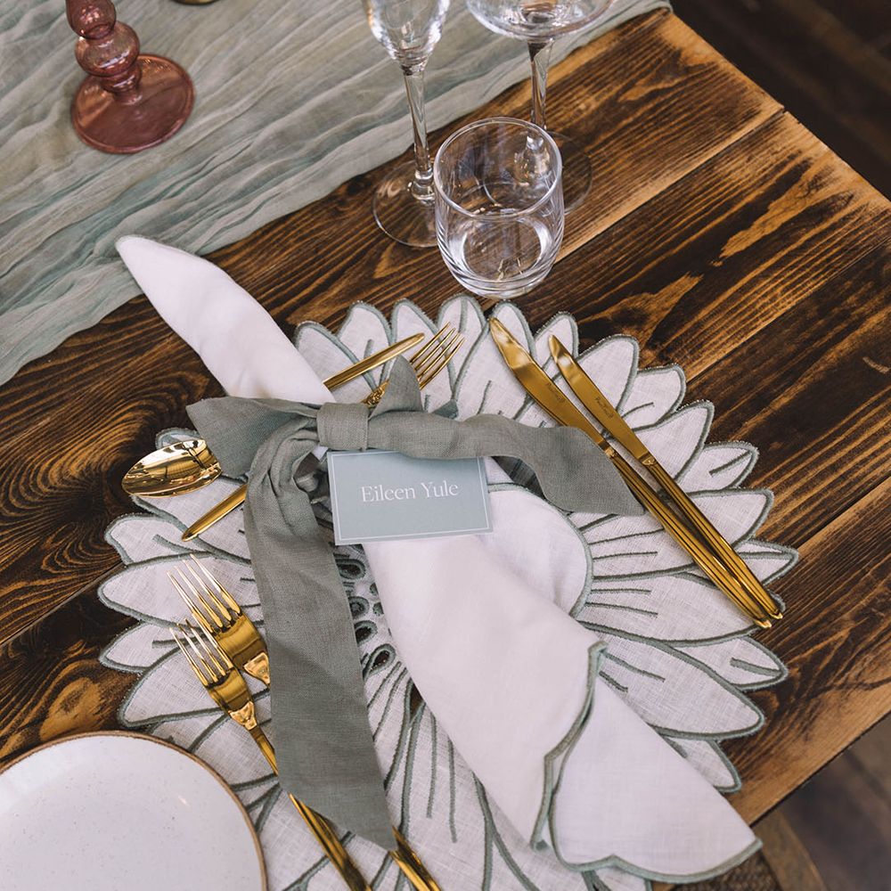 White and sage green floral place mat with gold cutlery, white napkin and place name 