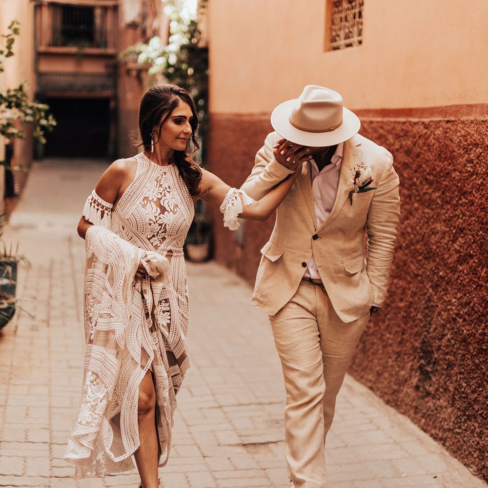 The bride wears a lace bridal gown with the groom wearing a wedding hat that matches the suit 