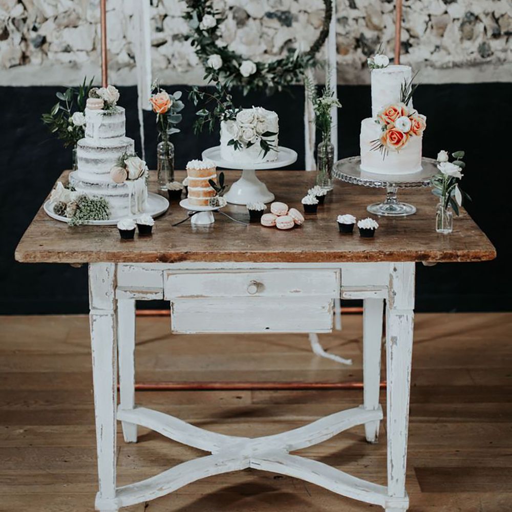 Wooden dessert table with three rustic wedding cakes with cupcakes decorated with white frosting and macarons 