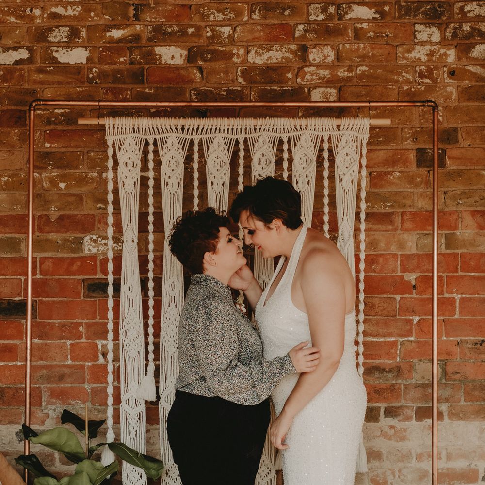 LGBT Wedding with two brides standing in front of a macrame backdrop