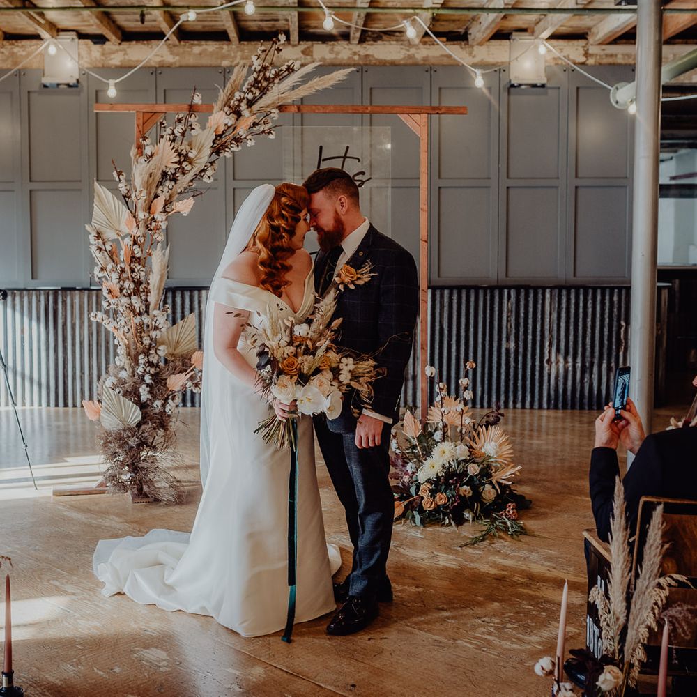 Bride and groom standing at the wooden altar decorated in dried flowers 
